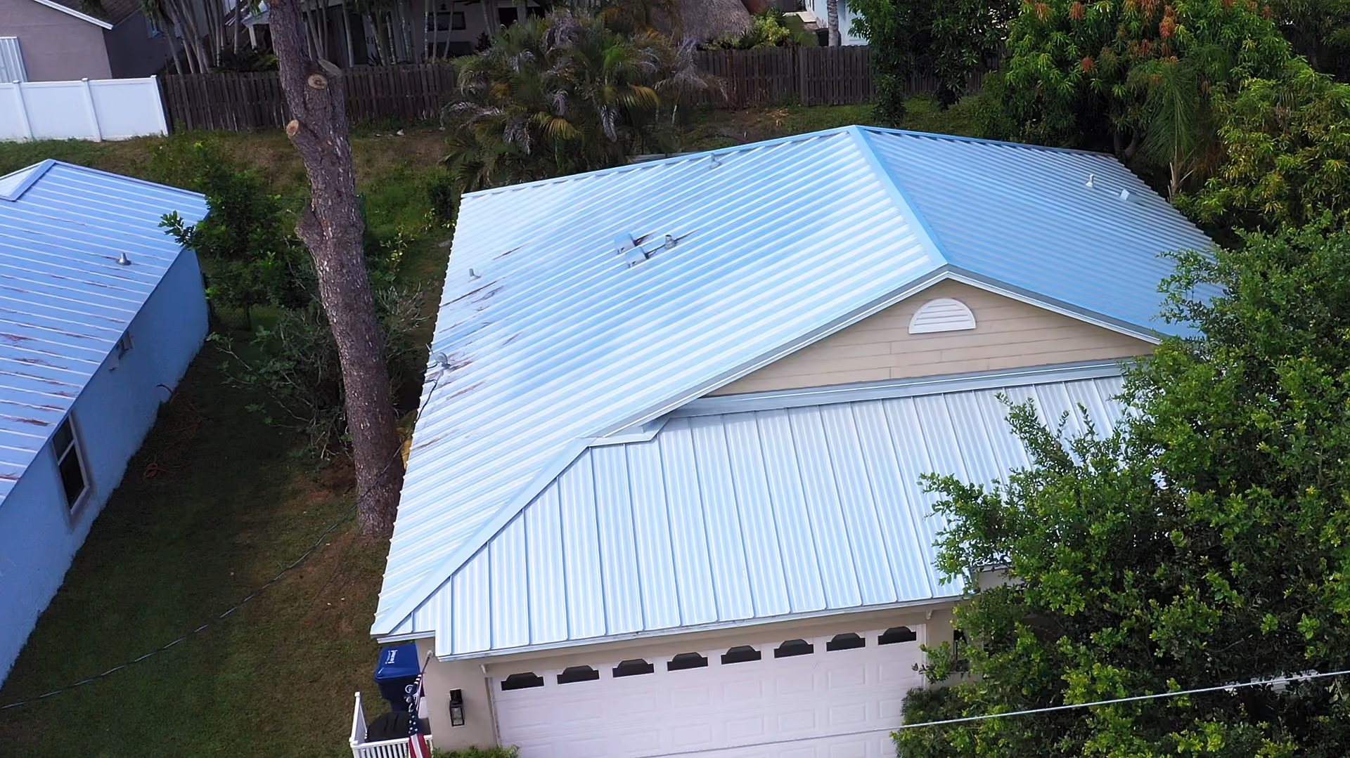 A silver ribbed metal roof with a half-round gable vent, seen from above with a tall pine beside the house