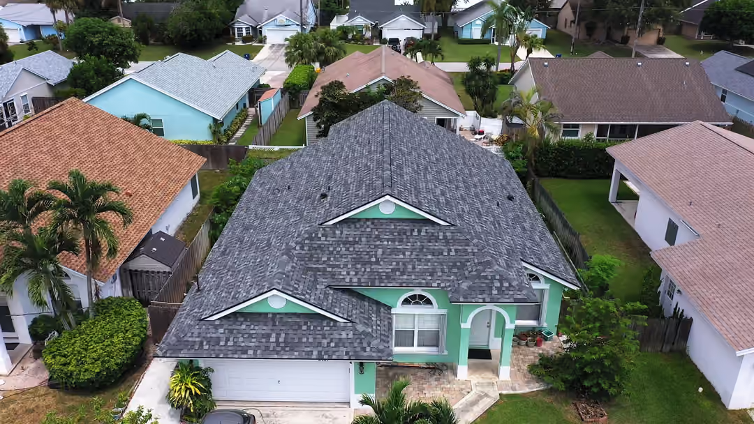 A gray blended shingle roof over a single-story house with an arched entry portico, terracotta tile roofs on the homes to either side