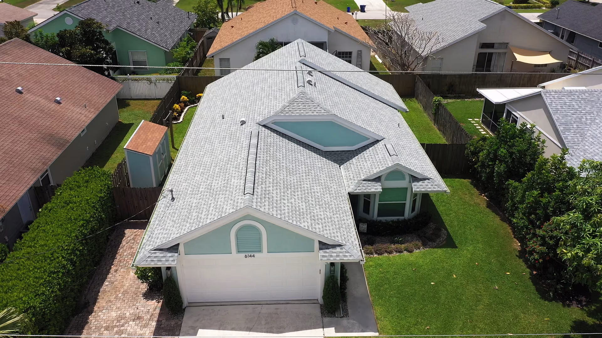 A pale sage home under a light gray architectural shingle roof, with arched gable vents above the garage and the bay window