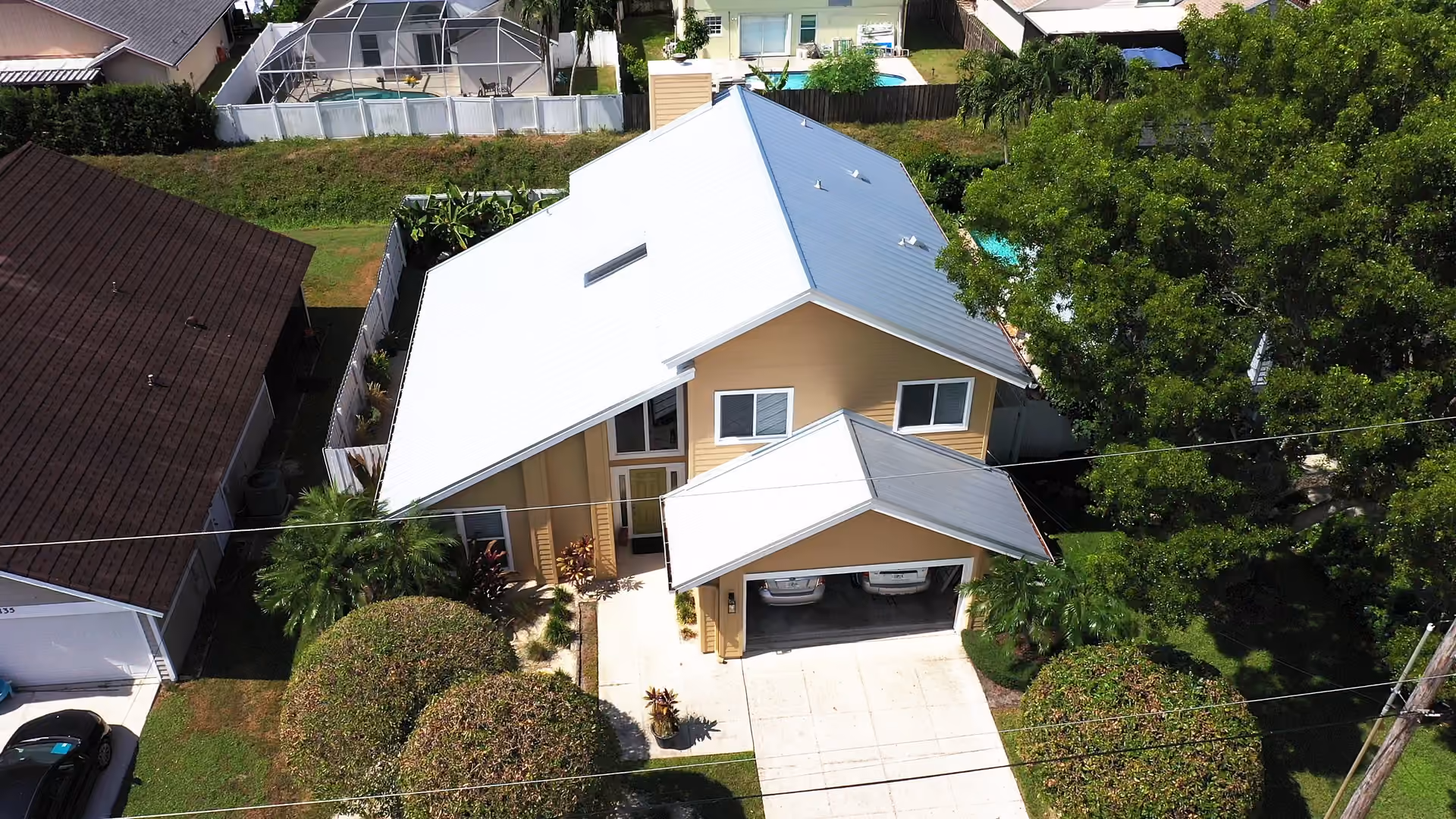 A tan two-story house under a white standing seam metal roof, with a matching metal carport covering the driveway