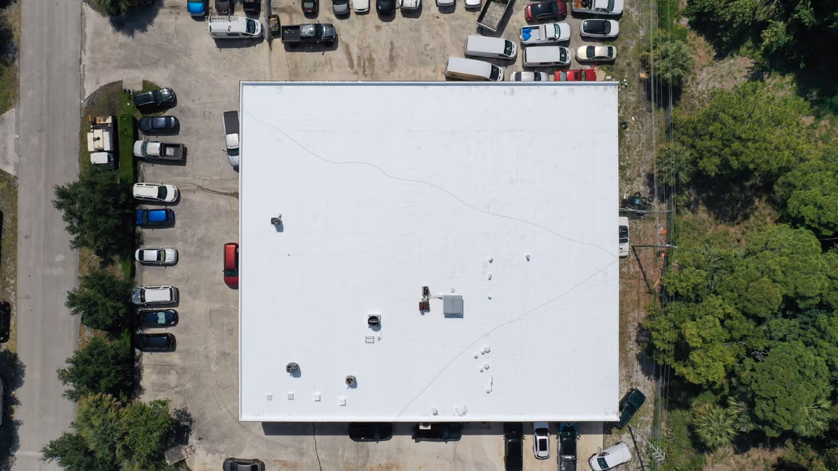 A white flat roof on a commercial building seen from directly above, with rooftop units near its center and cars and vans parked on three sides
