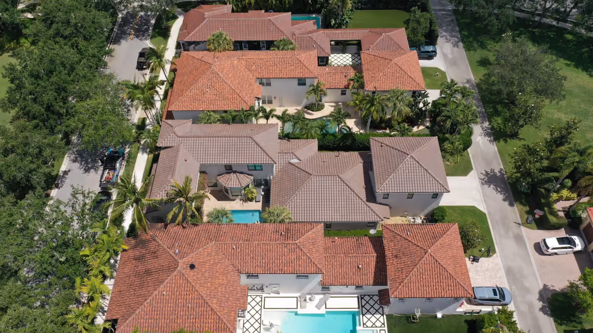 Terracotta tile roofs across a row of estate homes seen from above, pools and paver drives between them