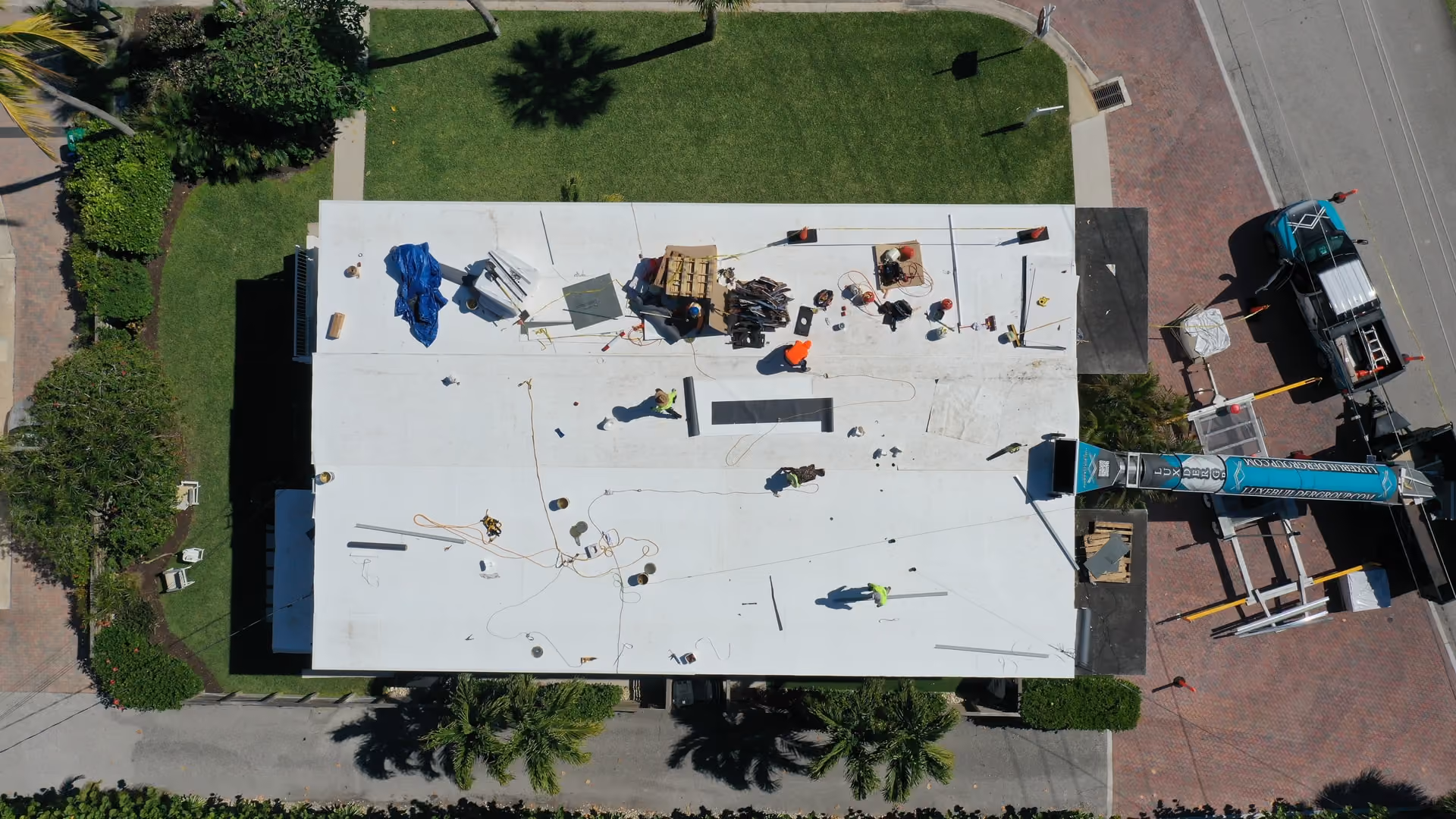 Crew working across a white flat roof on a two-story condo building, seen from directly above with staged boards along the field