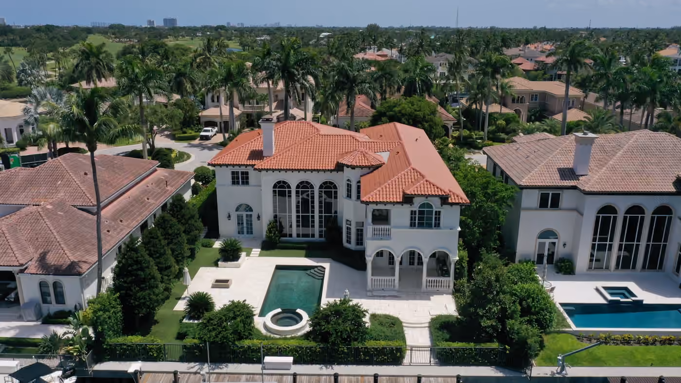 A large white Mediterranean house under a new terracotta barrel-tile roof, with a two-story arched window wall, an arcaded loggia, and a lap pool and spa on the terrace below