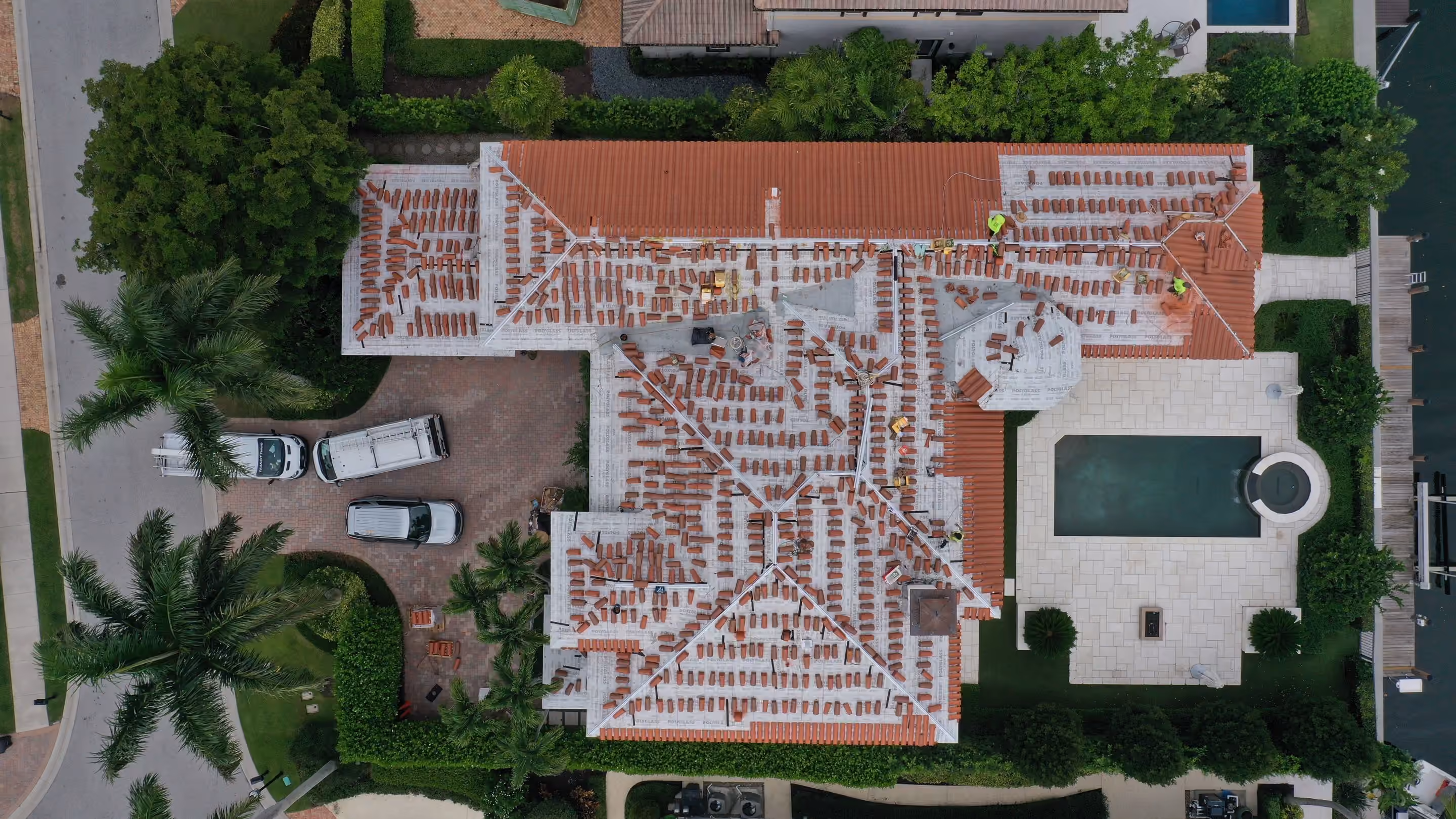 A large estate seen from directly above with new terracotta barrel tile stacked across the roof for setting, and a paver motor court at the front of the house