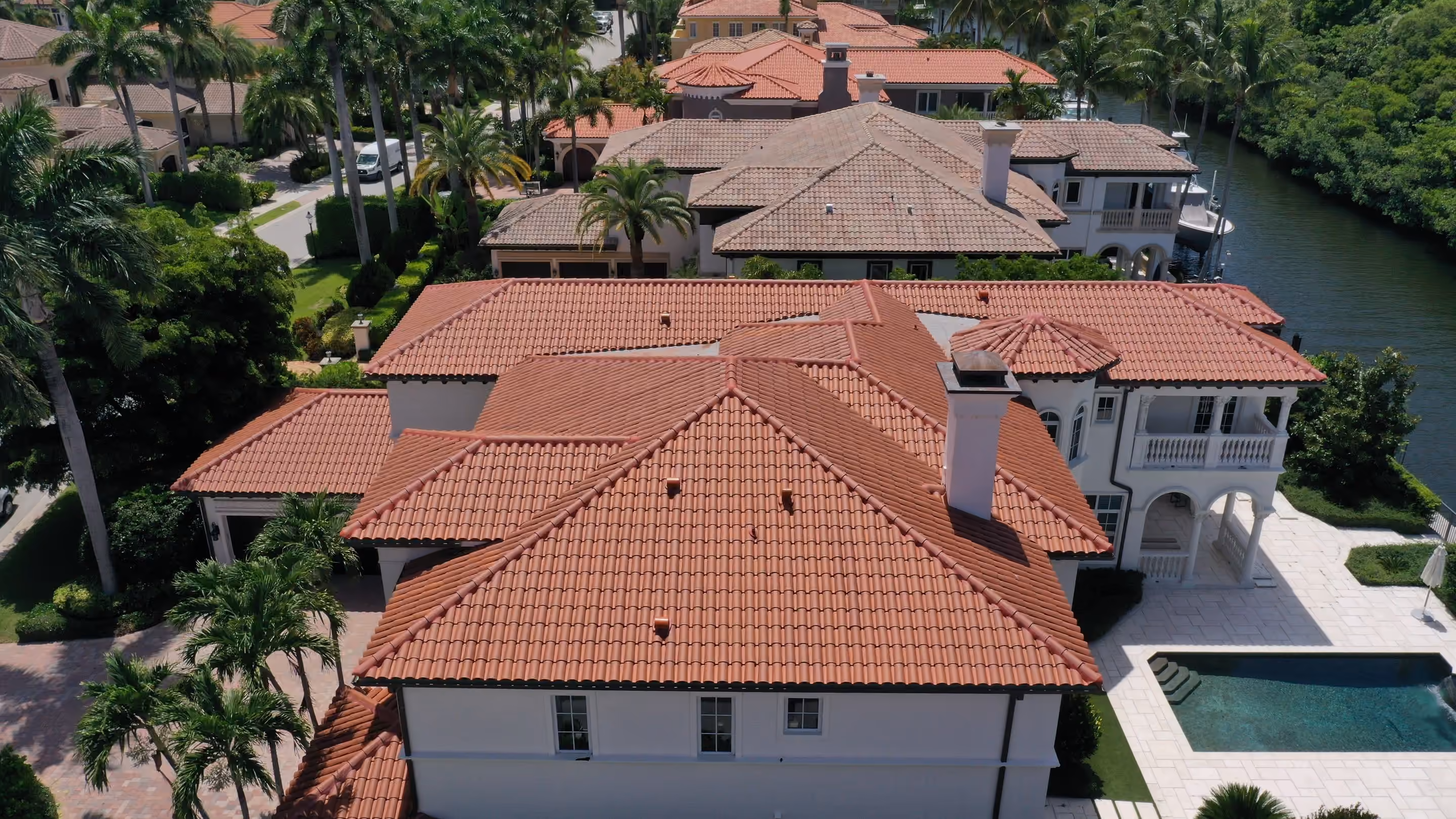 A large estate under fresh terracotta barrel tile seen from the air, with a pool on the terrace and a boat lift on the Intracoastal behind the house