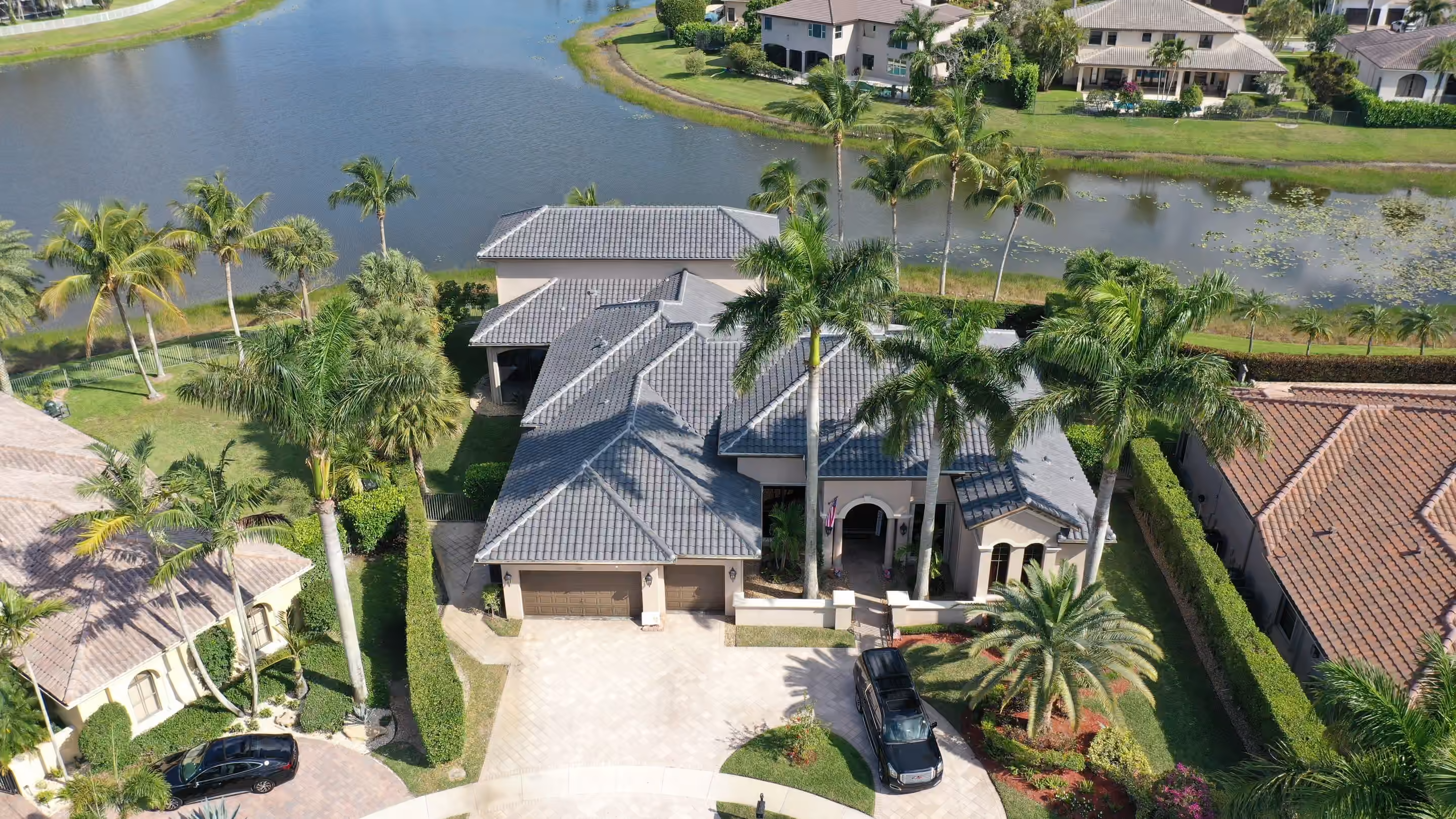 A lakefront home under a new gray tile roof, royal palms across the front and a paver drive curving to the garage