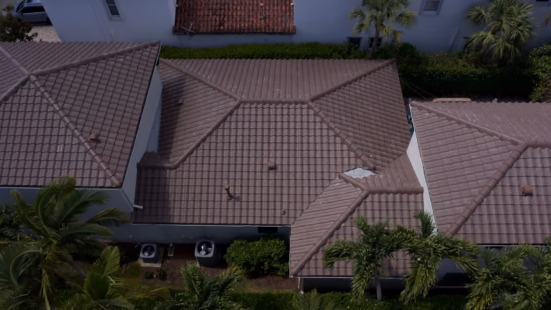 A brown tile roof photographed from directly above, its hips and valleys meeting across several planes, pipe vents standing up from the field and one small exposed patch beside a valley