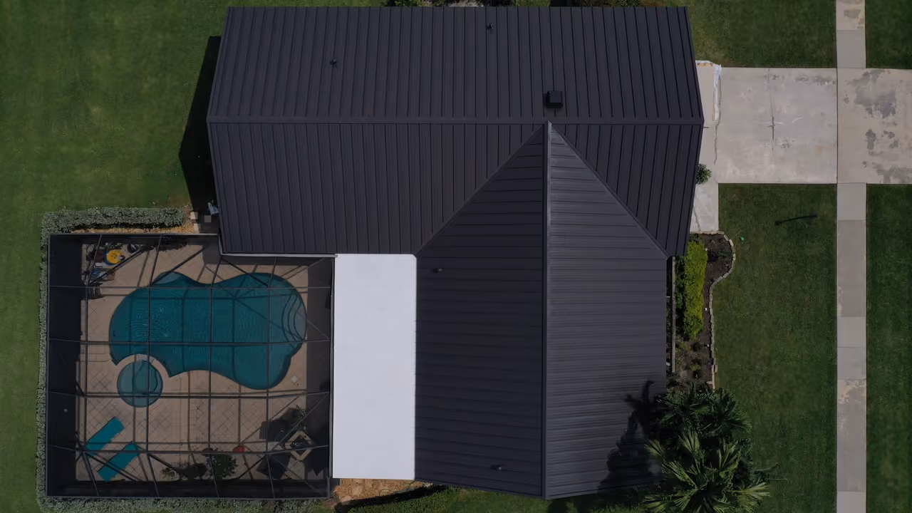 A black standing seam roof seen from directly above, panel lines meeting at the hips, with a screened pool enclosure below