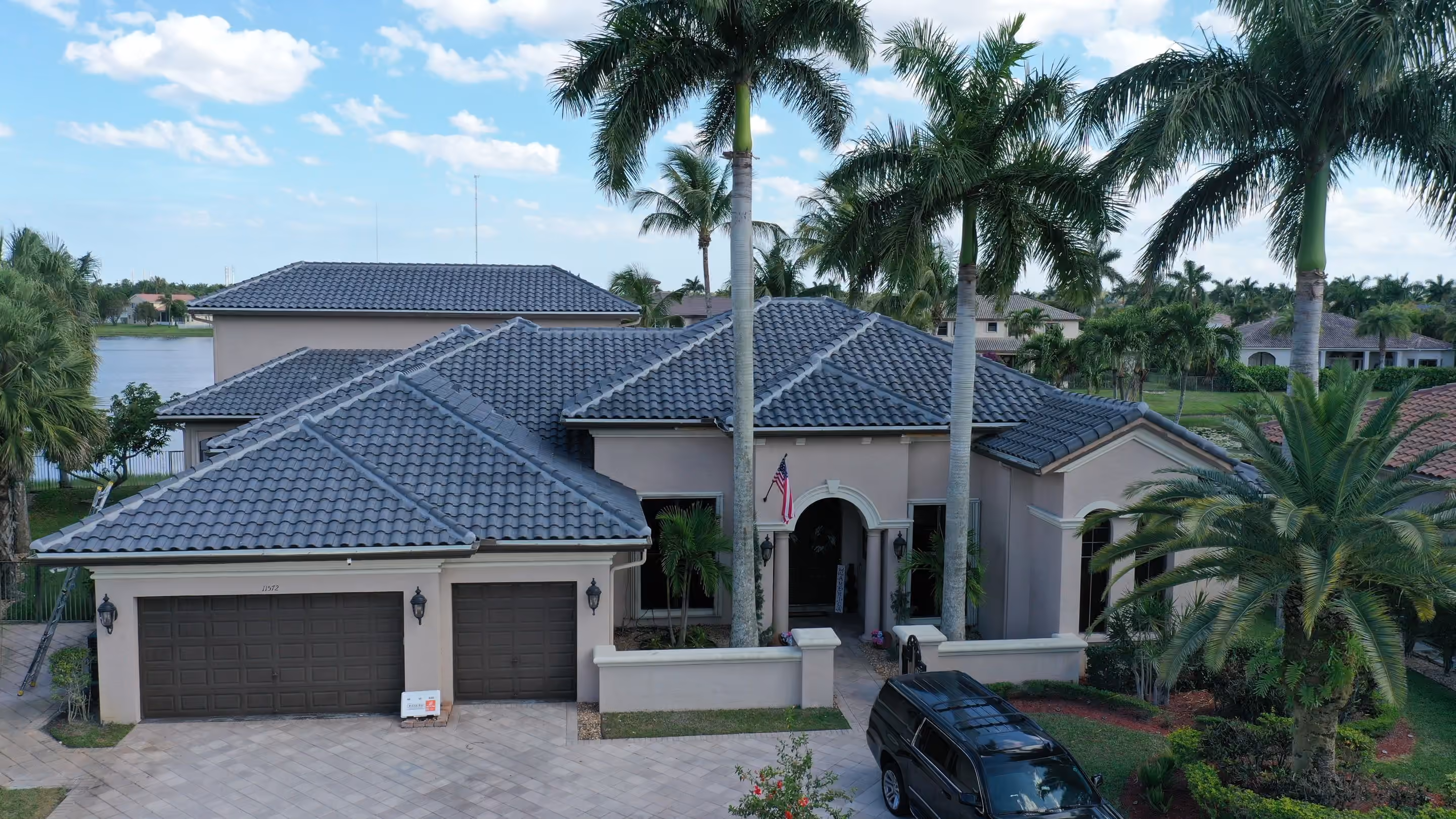 A single-story house with a gray tile roof, a paver driveway and royal palms across the front, photographed from the street side