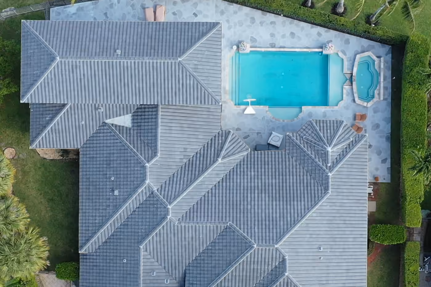 A gray tile roof across a large estate seen from directly above, with a rectangular pool and spa on the terrace beside it