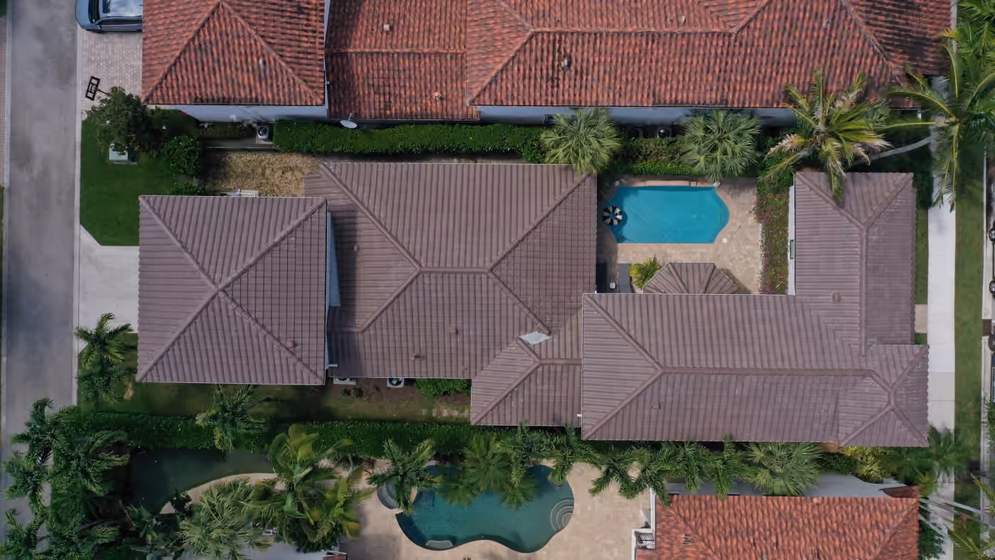A dark flat-tile roof across a large estate seen from directly above, with two pools on the surrounding terraces