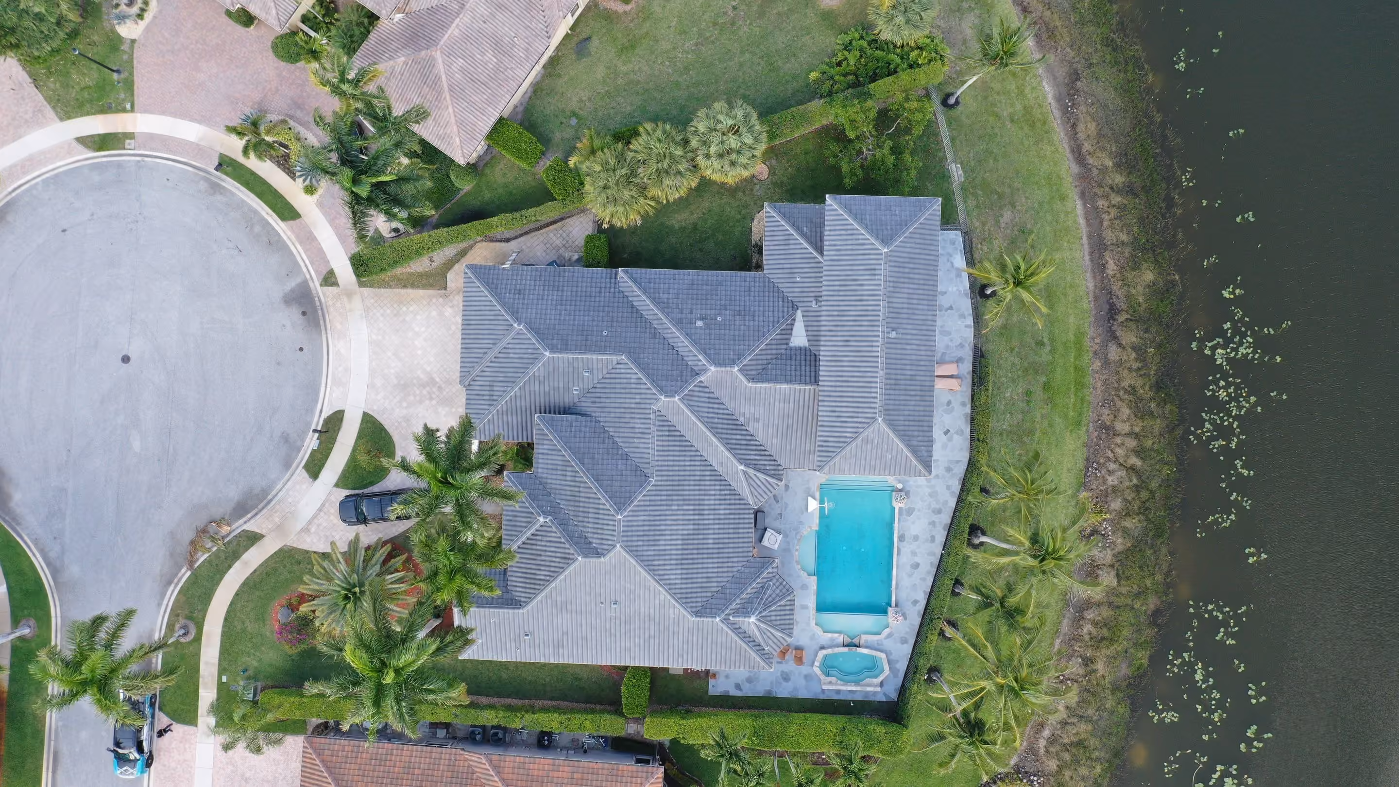 A gray flat tile roof photographed straight down on a lakefront house, with a pool and spa on the terrace and the lake edge beyond the lawn
