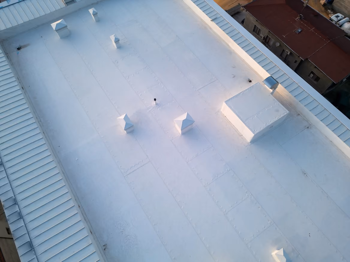 A white flat roof seen from above, with square vent hoods and a raised unit on the roof and standing seam metal along its edges.